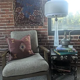 Handwoven Nadia Moroccan cactus silk throw pillow in deep brown with diamond embroidery, displayed on a chair with brick wall